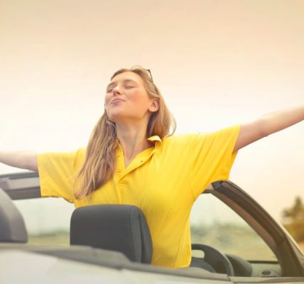 A cheerful woman in a yellow shirt enjoys freedom on a sunny drive in a convertible.