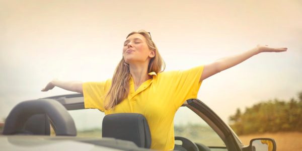 A cheerful woman in a yellow shirt enjoys freedom on a sunny drive in a convertible.